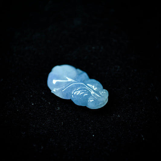 A bluish-purple jadeite carving in the shape of a goldfish, placed on a black velvet background.
