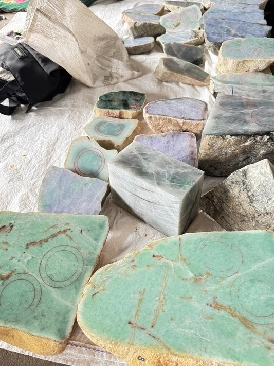 Natural jadeite rough stone slabs showing geological cracks marked with red circles, including rare apple green jadeite pieces demonstrating why flawless bangles are valuable