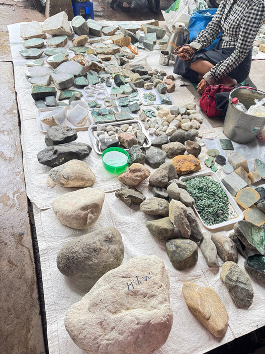 Raw jade stones and rough emerald displayed on white cloth at Myanmar jade market with vendor