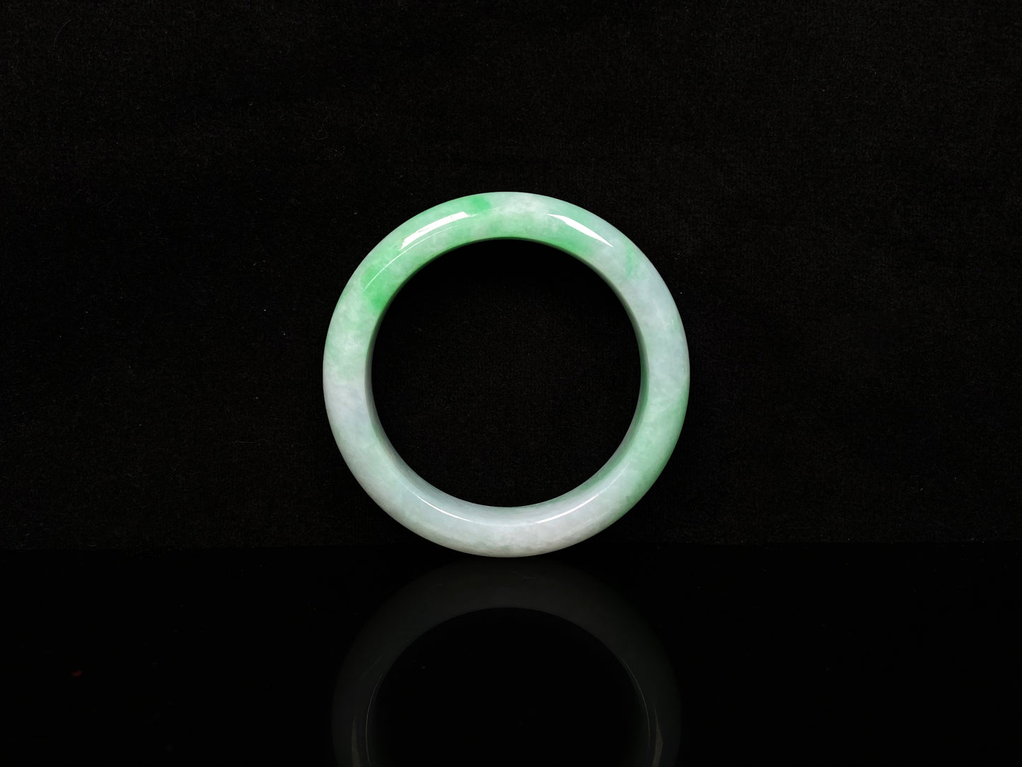 A white field with floating green hues jadeite bangle.