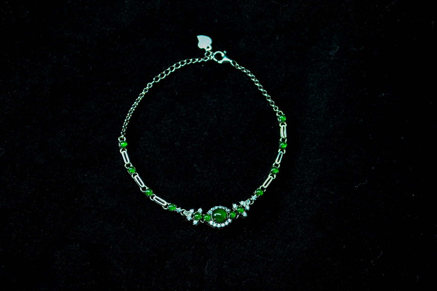 Silver bracelet with green gemstones on a black background