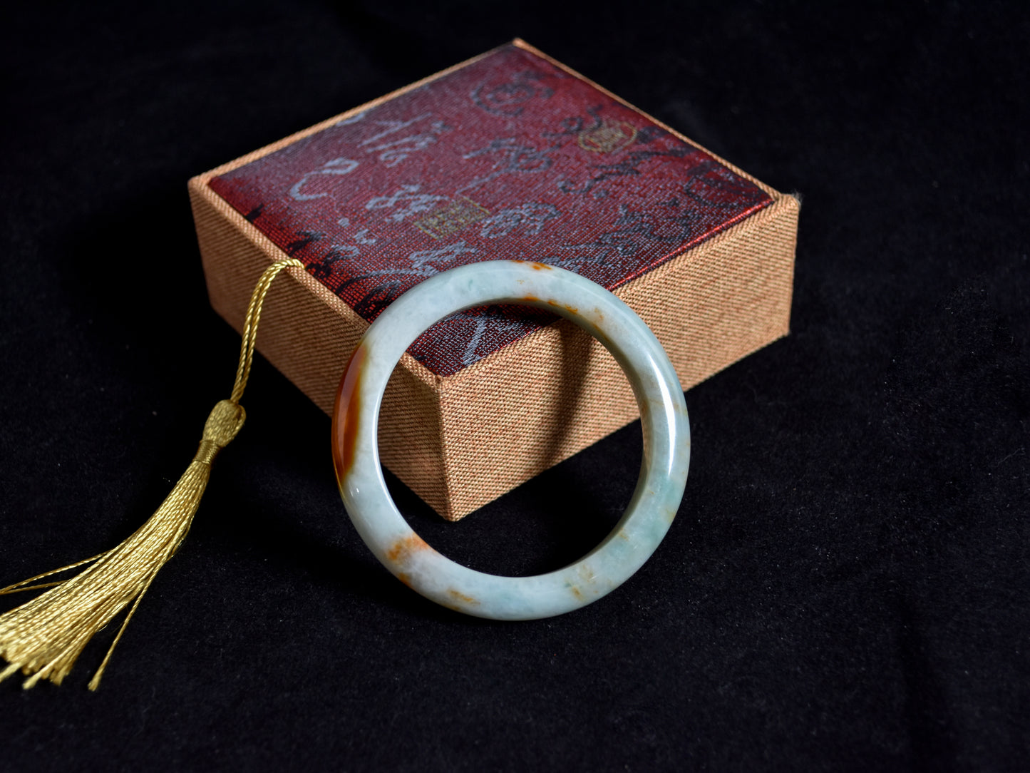 Green jade ring on a textured box with a gold tassel against a black background