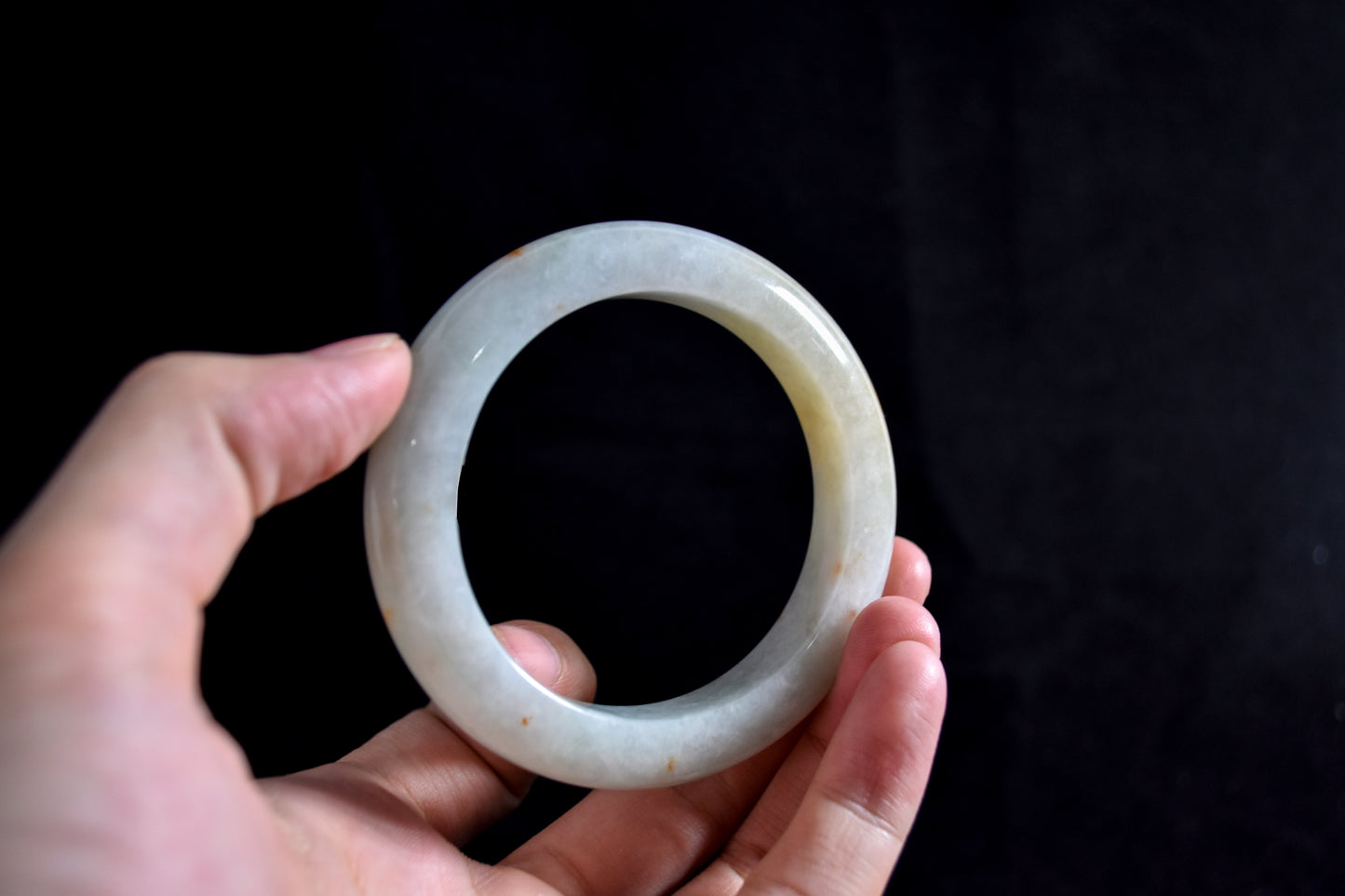 Hand holding a white jade ring against a dark background