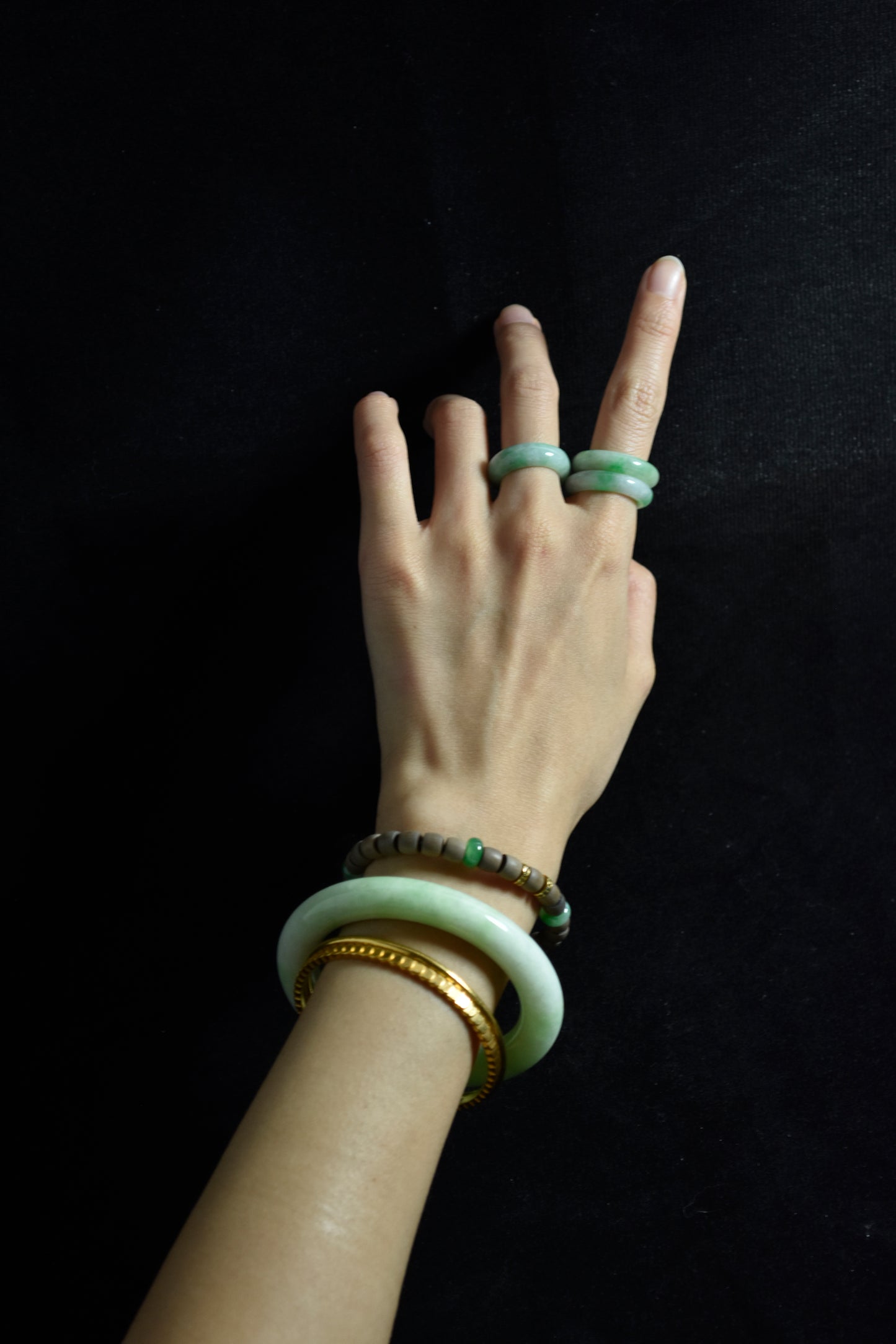 Hand wearing multiple bracelets and rings on a black background