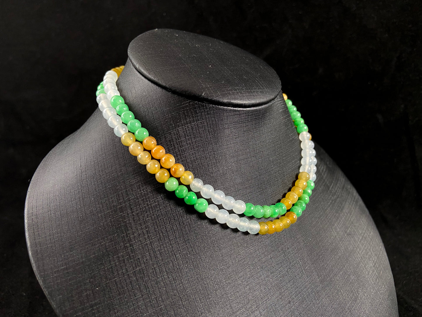 This jade bead strand alternates clusters of apple green, yellow, transparent white, and brown beads in a rhythmic color pattern.