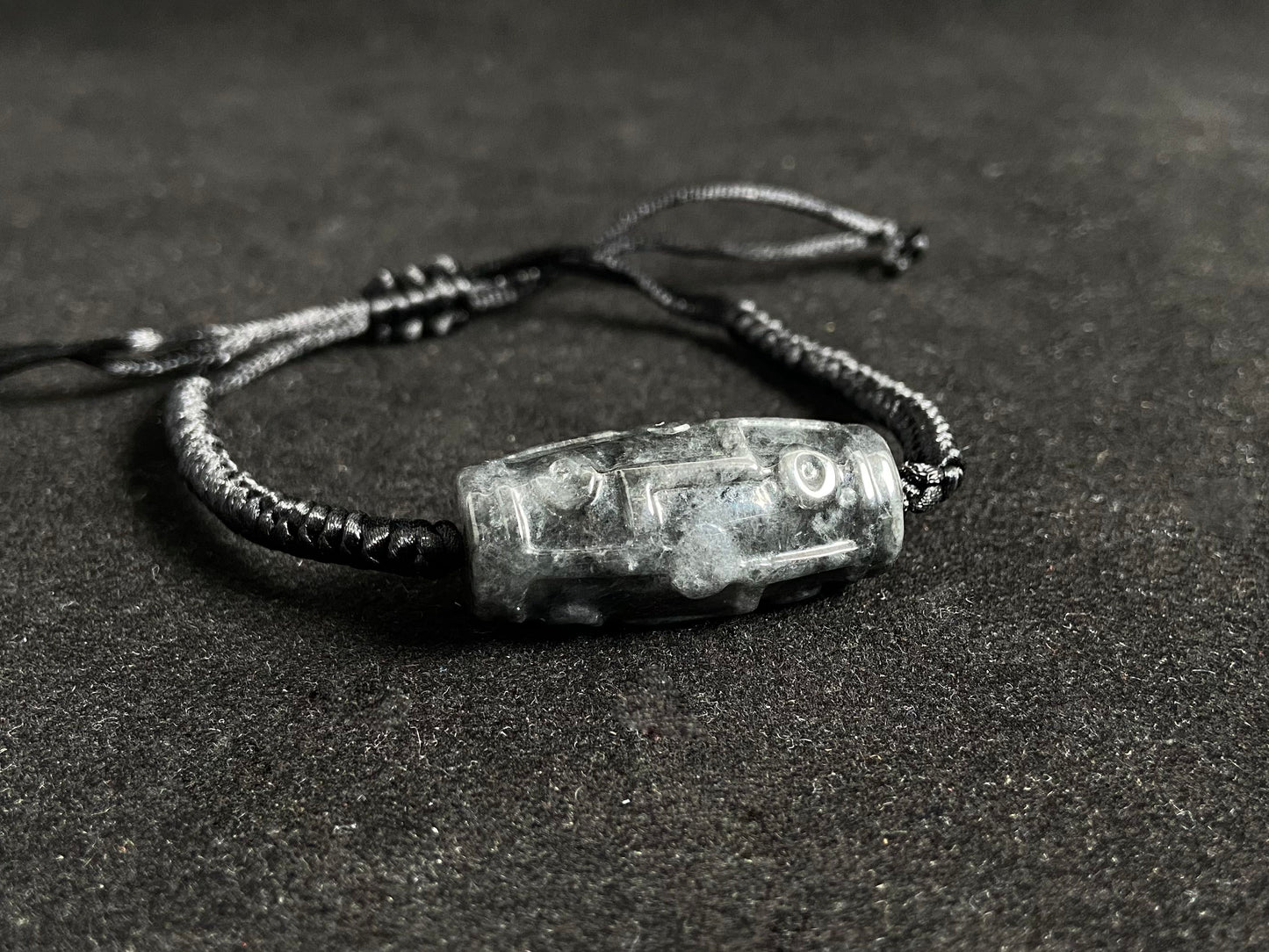 This braided bracelet combines a black cord with smooth gray "Lulutong" jade beads, creating a timeless and meaningful accessory.