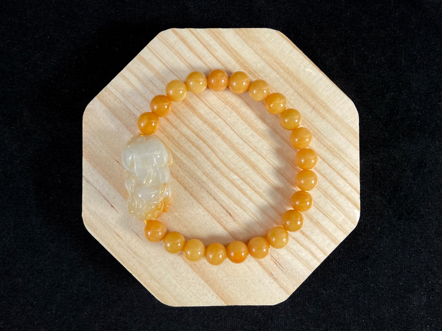 A jade bead strand featuring a white based gold flecked pixiu charm and yellow beads.