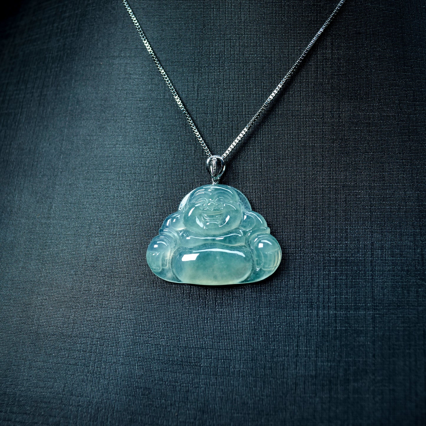 Clear Buddha pendant on a chain against a dark fabric background