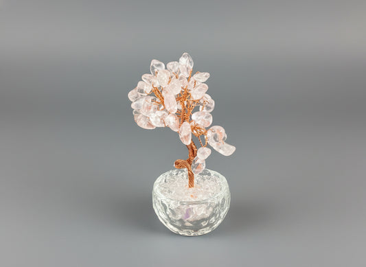 A rose quartz crystal tree in a clear glass pot.