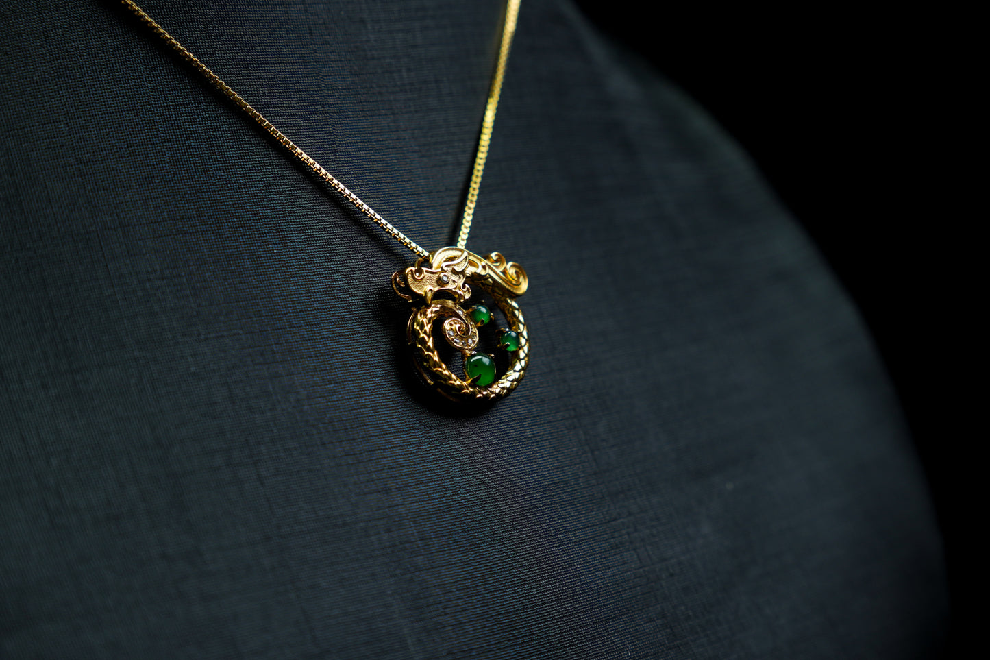 Gold necklace with a green gemstone pendant on a dark fabric background