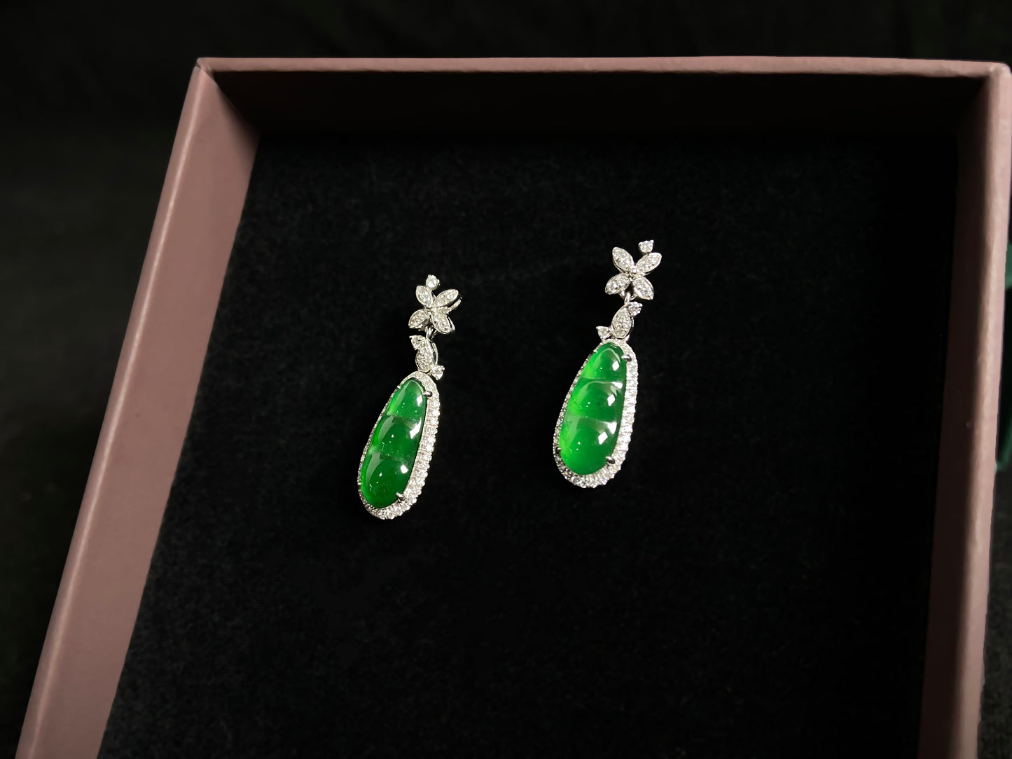 These elegant earrings feature imperial green jadeite lucky beans, each meticulously set in 18K gold with secure prong settings.