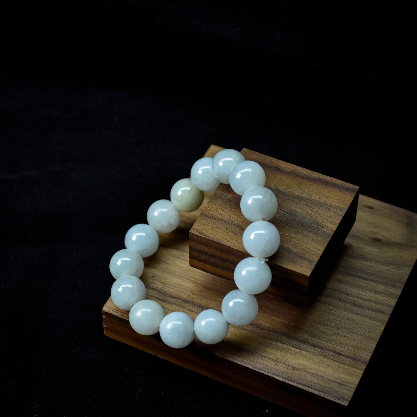 White beaded bracelet on a wooden stand against a dark background