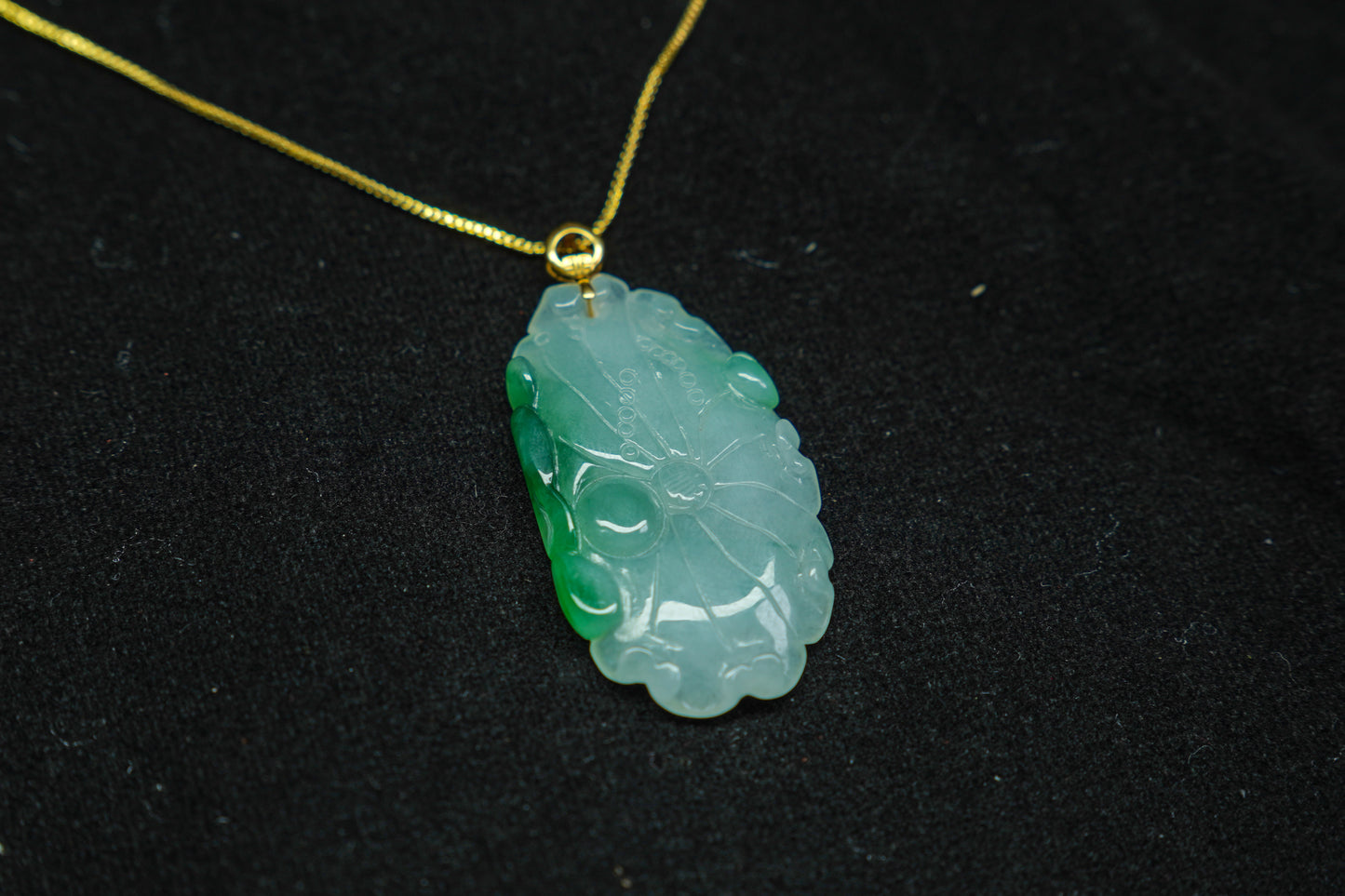 Green jade pendant on a gold chain against a black background