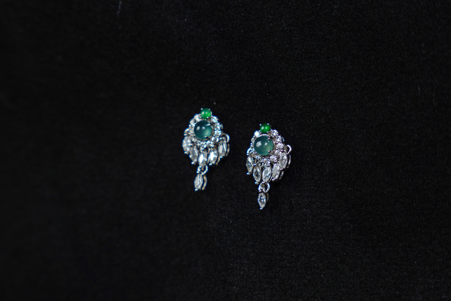 Pair of silver earrings with green gemstones on a black background