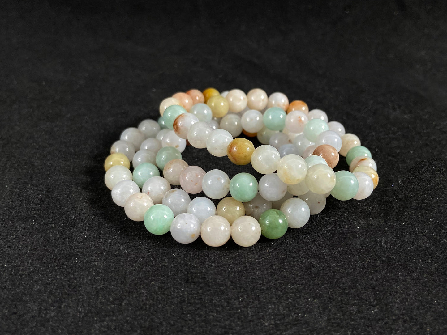 A jade bead strand featuring light green, tan, forest green, creamy white, and orange hues.
