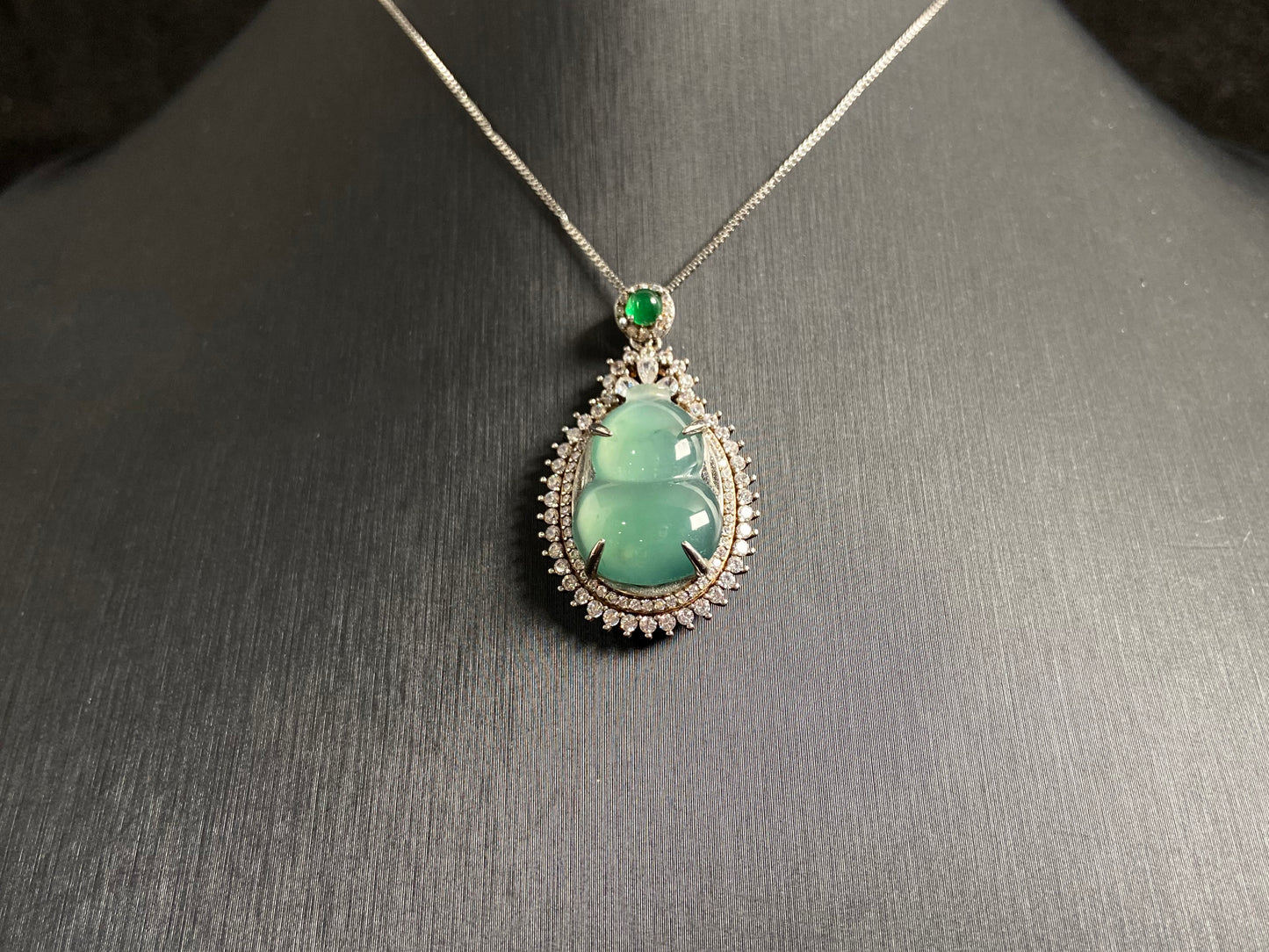 This jade pendant features a serene aqua green Hulu(gourd) accented with a regal imperial green jade bead, both elegantly set in 925 silver.