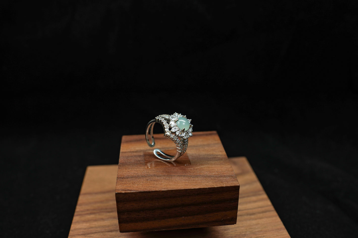 Silver ring with a green gemstone on a wooden stand against a black background