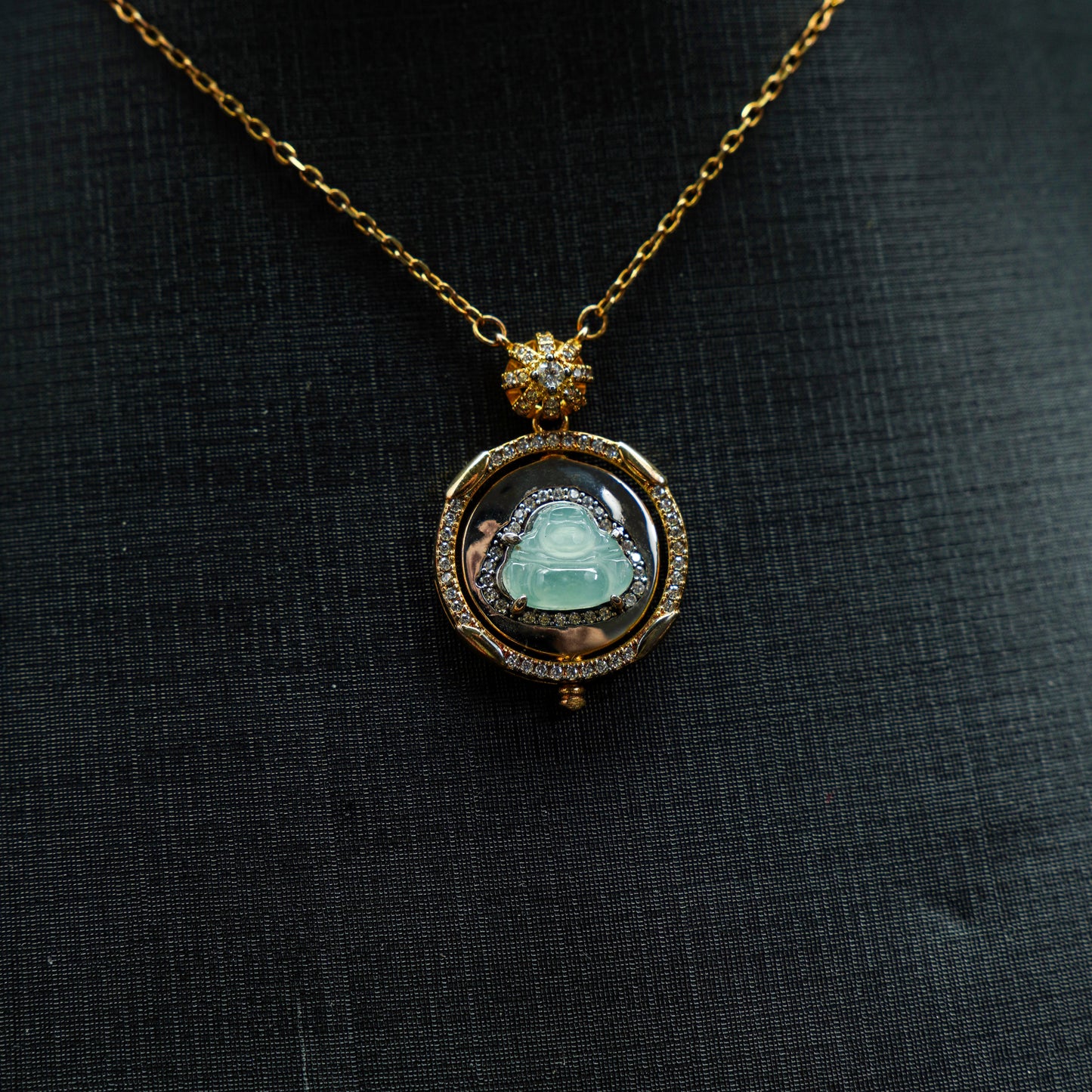 Gold necklace with a pendant featuring a green gemstone on a black fabric background