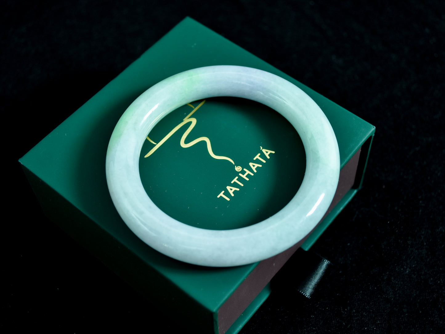 White bracelet on a green box with 'Tathata' branding against a dark background