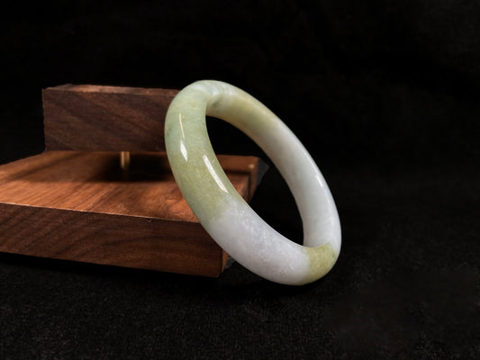 A creamy white jadeite bangle adorned with splashes of yellow-green.