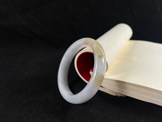 A creamy ivory jade bangle delicately kissed by two strokes of sunlit gold.
