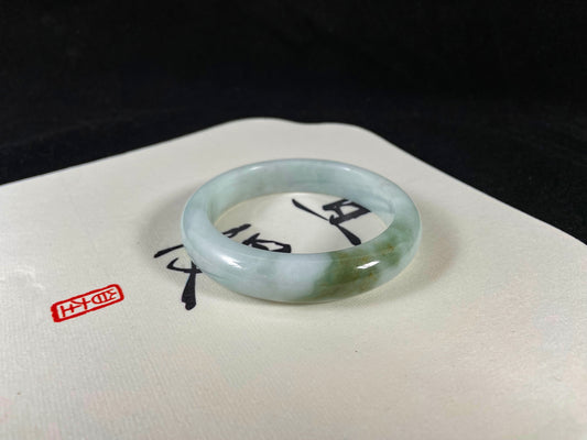 A pearl-white jade bangle embraced by a soft green mountain-water gradient.