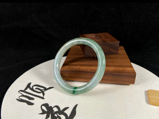 A green-veined jade bangle rests on a "Shun" fan against stacked wood.