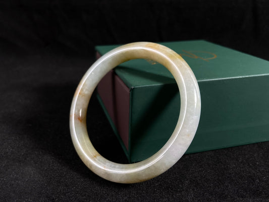 A white and green jade bangle with golden-brown specks, symbolizing harmony and fulfillment