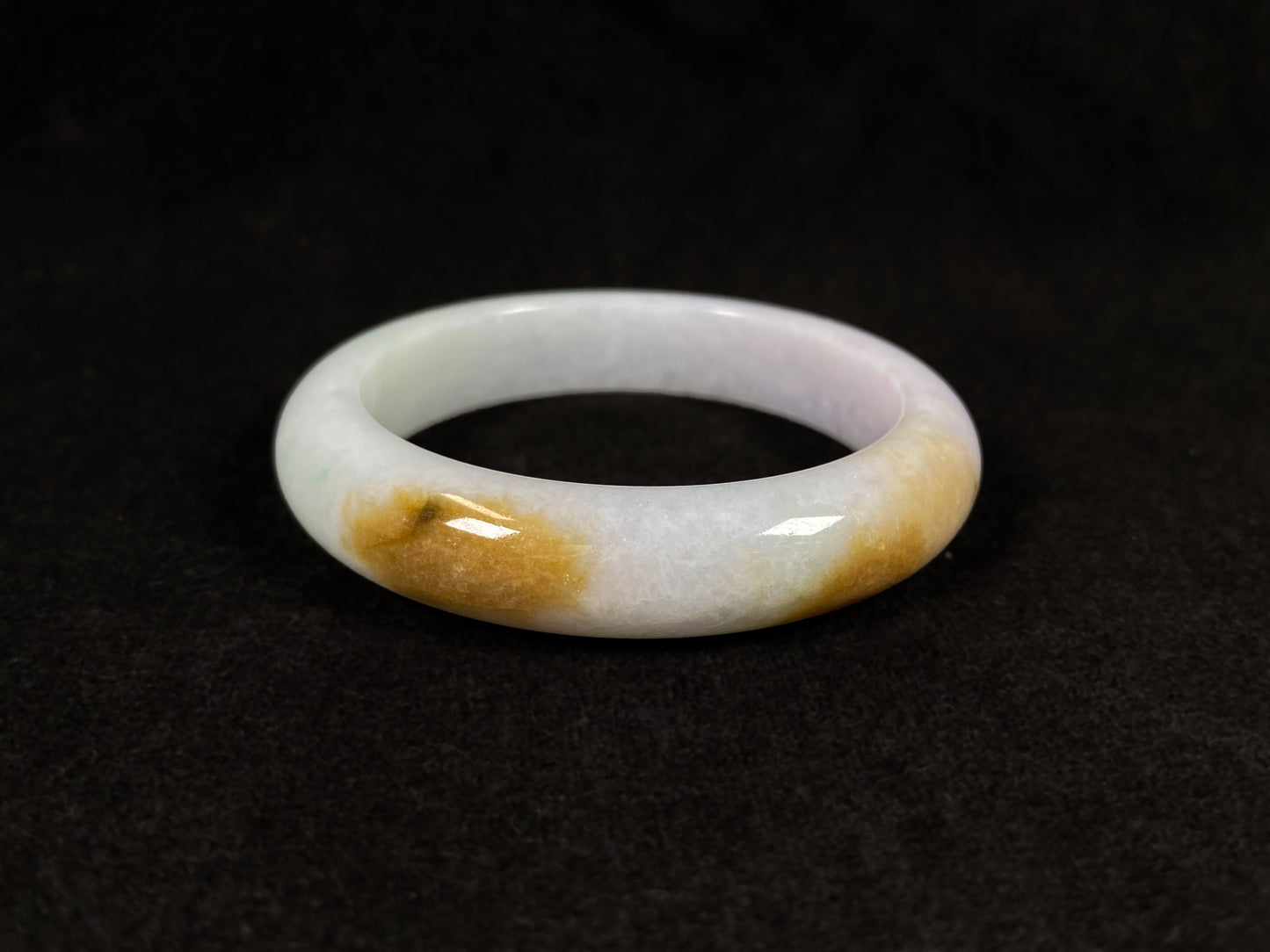 A white jadeite bangle featuring purple, gold, and light green tones.