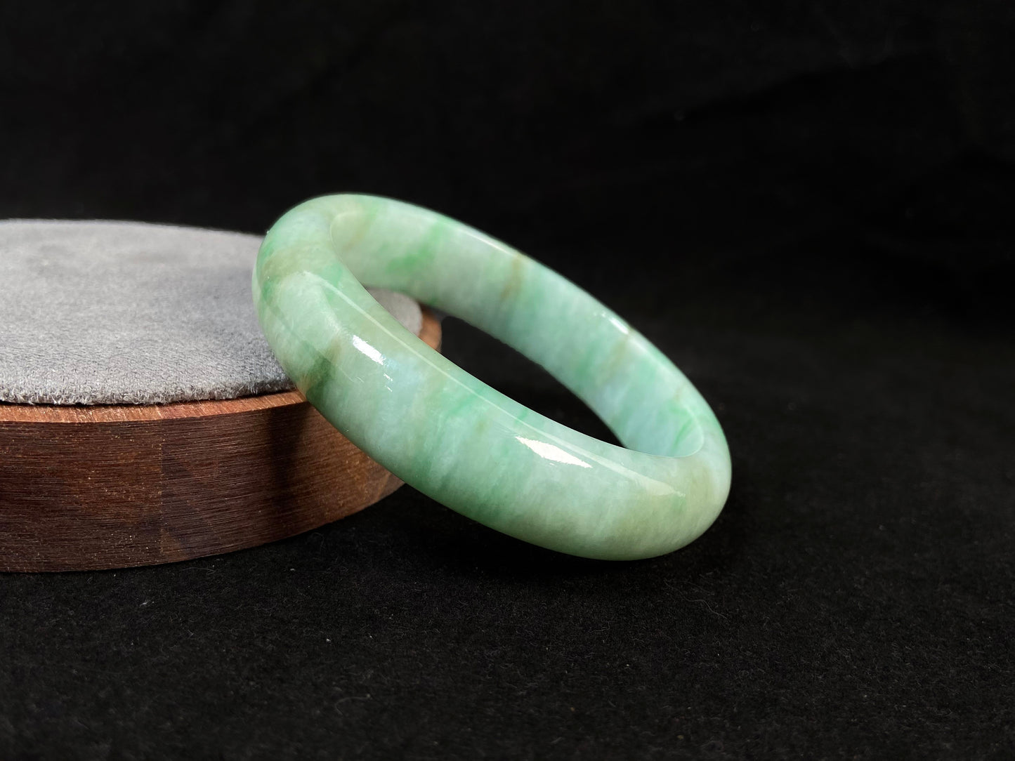 A white-based jade bangle adorned with soft green, deep green patterns and delicate gold speckles.