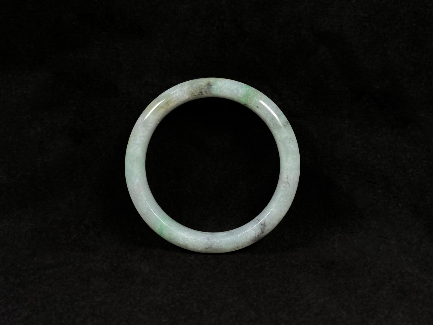 A white jadeite bangle with delicate light green veining and gray speckles.
