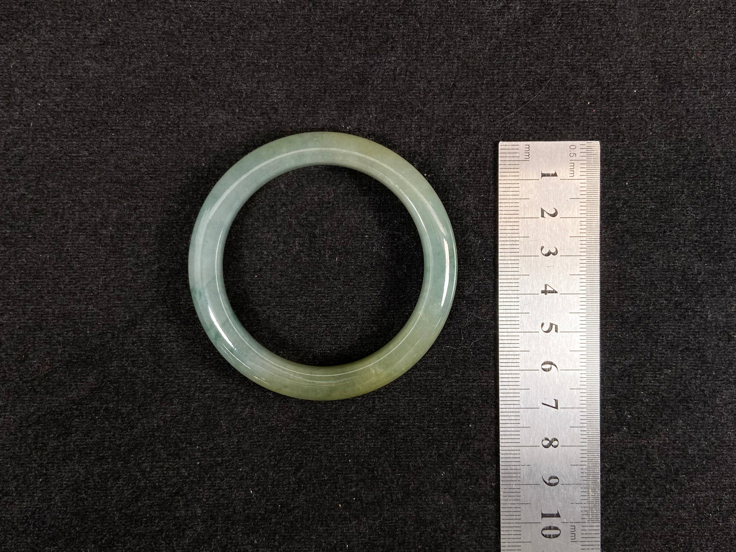 This jadeite bangle features a light green translucent base with floating green patches and integral areas of golden.
