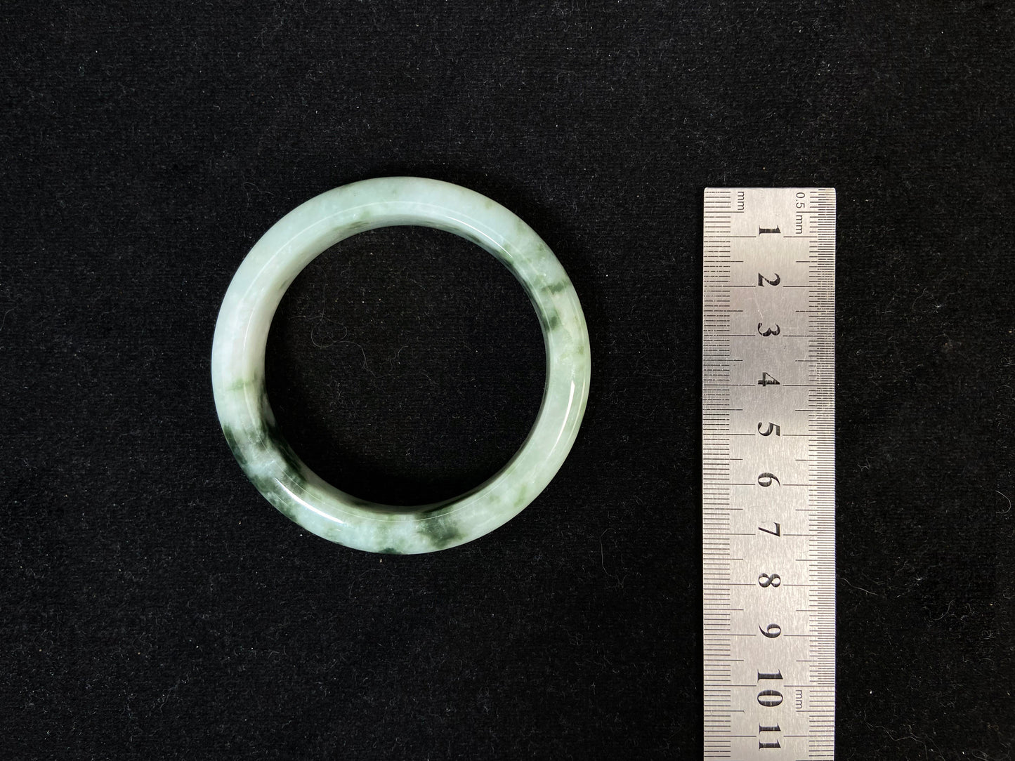 A milky white jade bangle with floating deep and light green patterns.