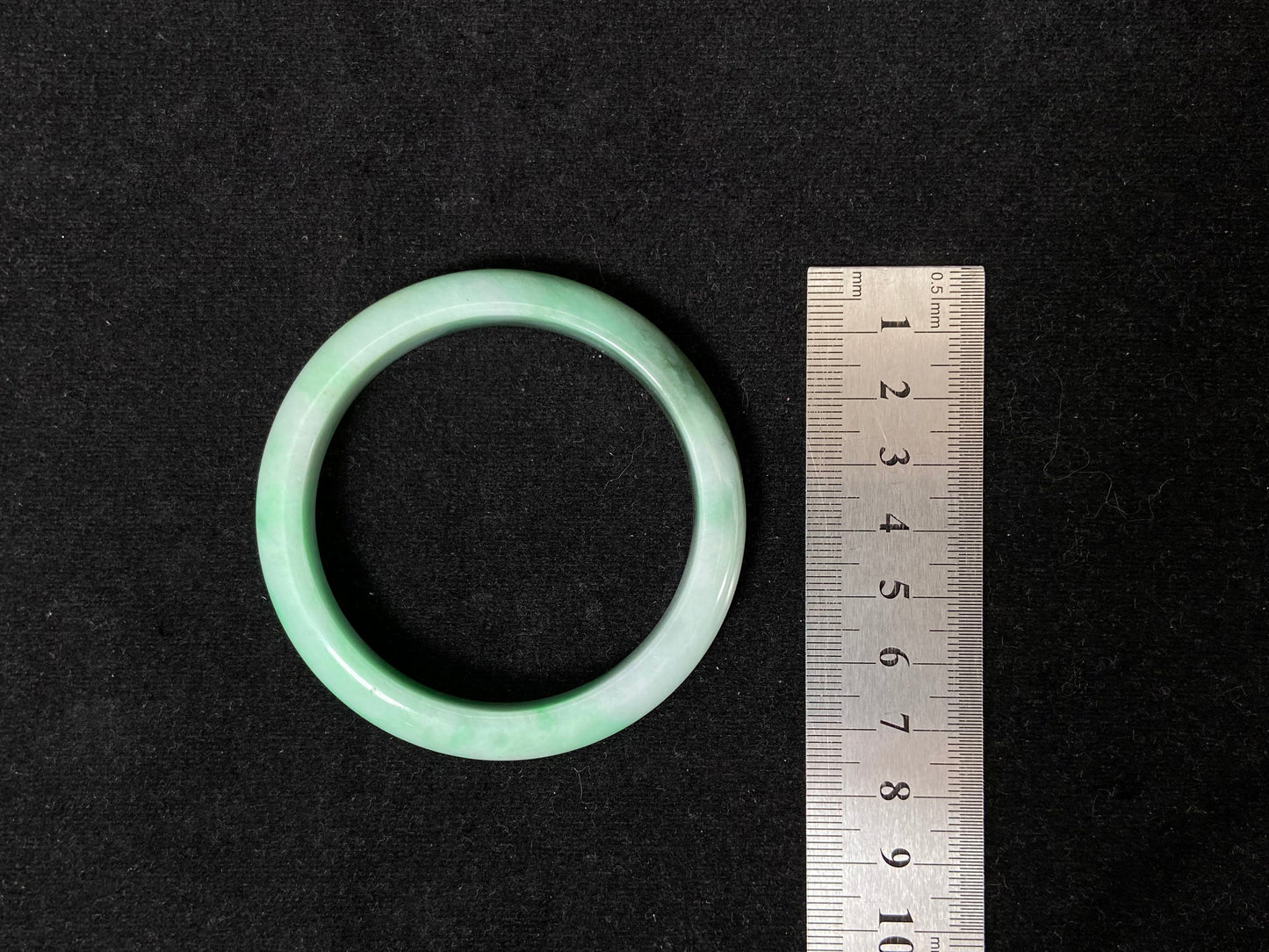 A jade bangle with a milky white base, featuring a large apple green section and a smaller olive green portion.