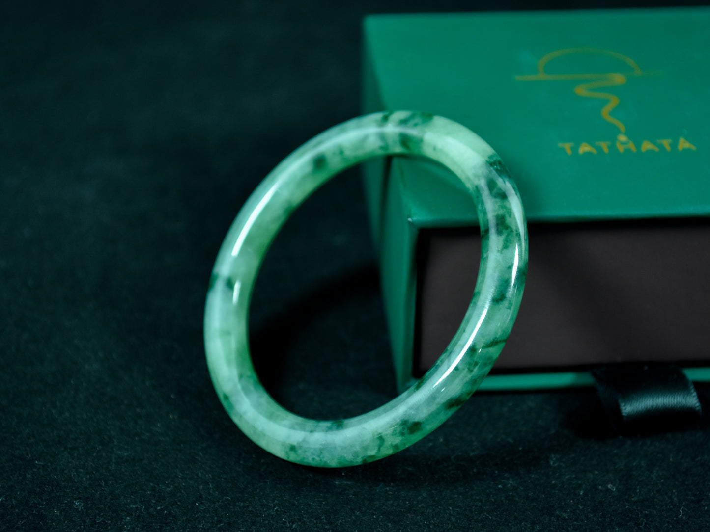 Green jade ring on a dark surface with a green box in the background
