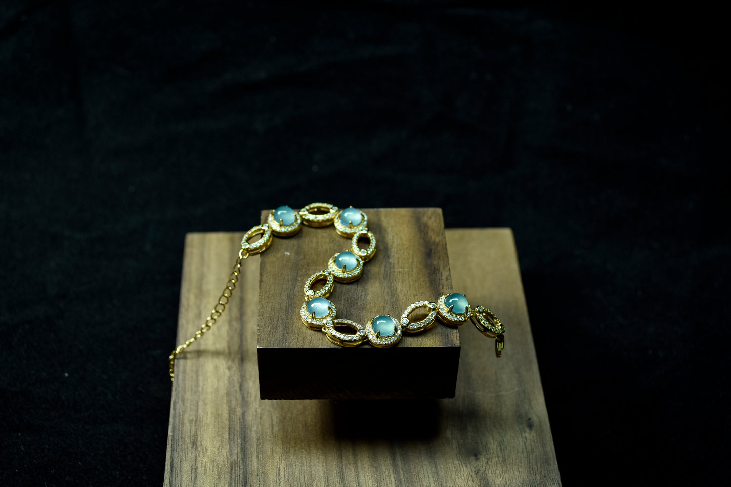Gold bracelet with blue stones on a wooden block against a dark background