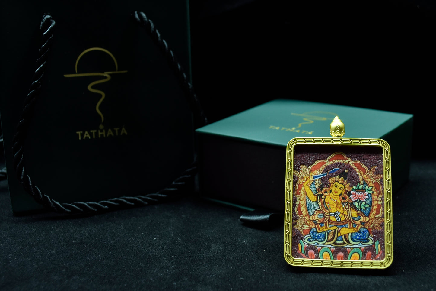 Decorative pendant with intricate design on a black background, featuring the brand 'Tathata'.