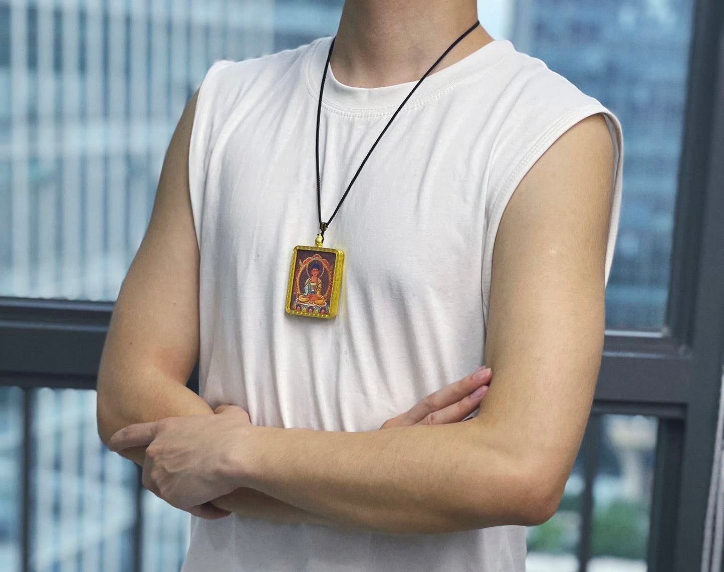 Person wearing a white sleeveless shirt with a necklace featuring a pendant, standing against a blurred cityscape background.