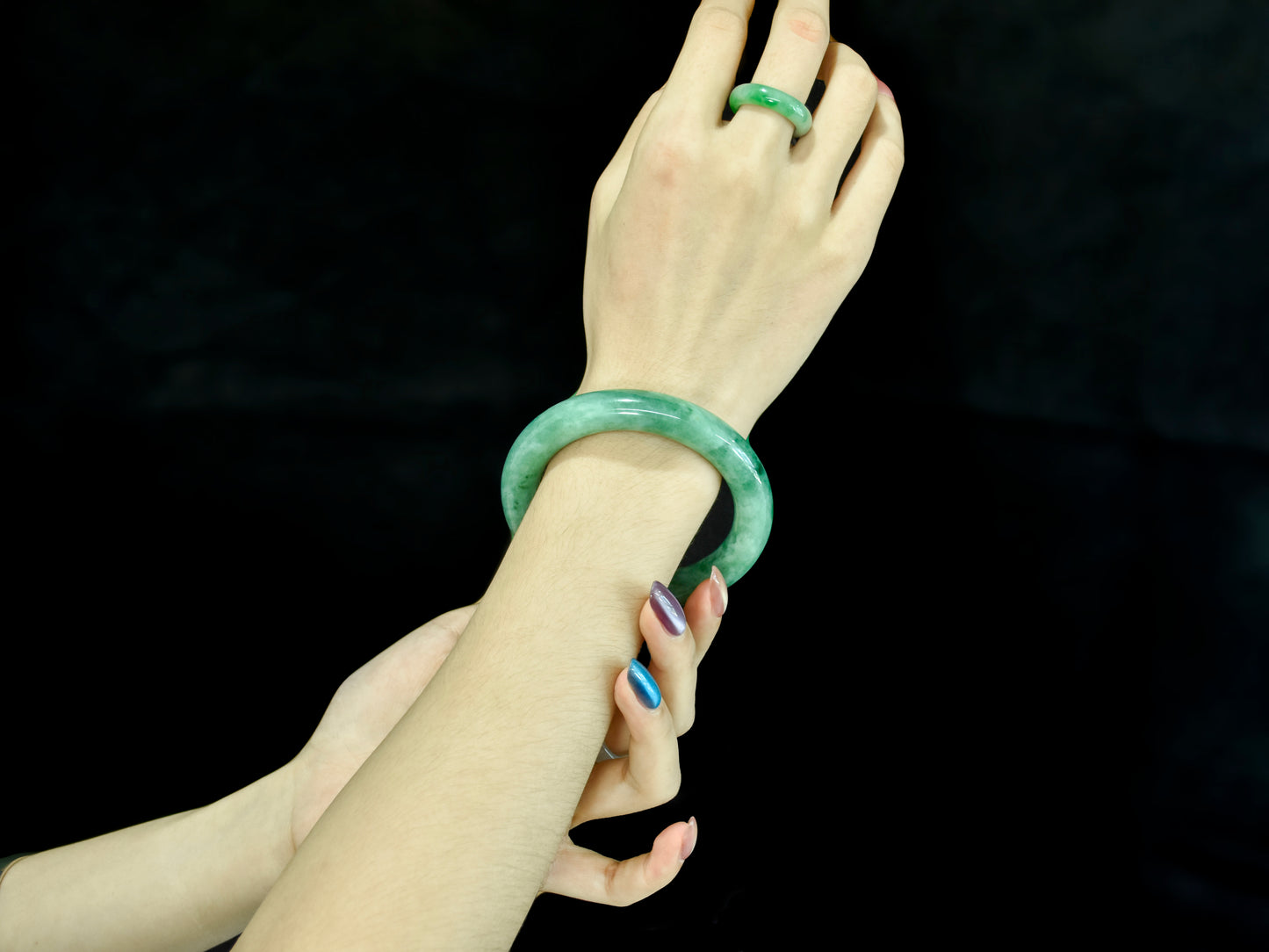 Two hands wearing green jade bracelets against a black background