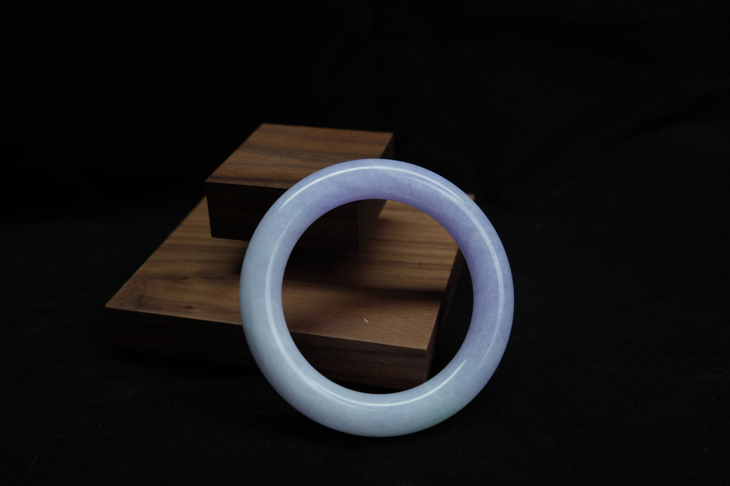 A natural violet jadeite round bangle displayed on a wooden stand, symbolizing elegance and serenity.