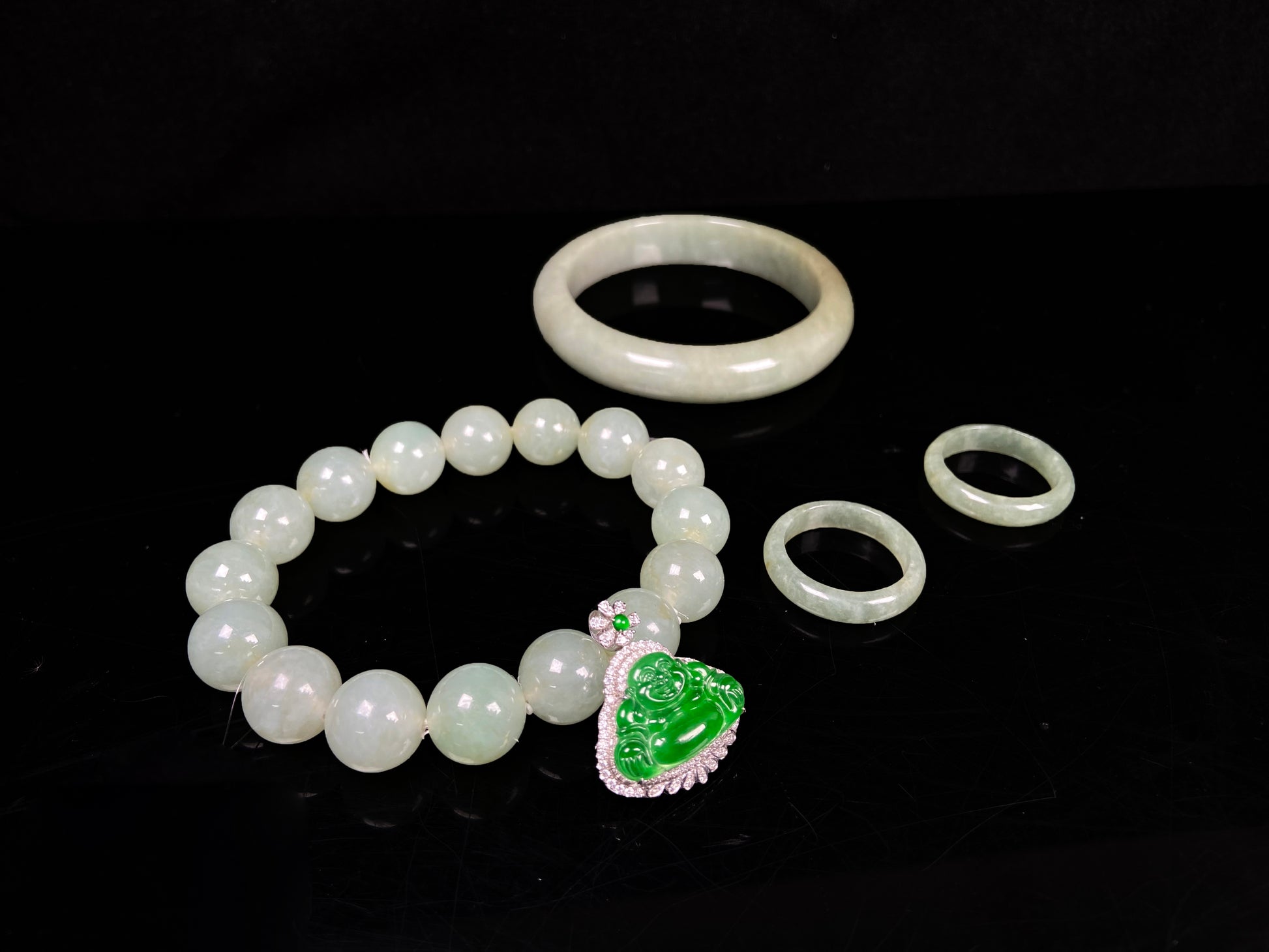 A set of four treasures of verdant glow Natural Burmese Jadeite. It includes a Buddha pendant, a round bangle, a beaded bracelet, and a plain band ring. 