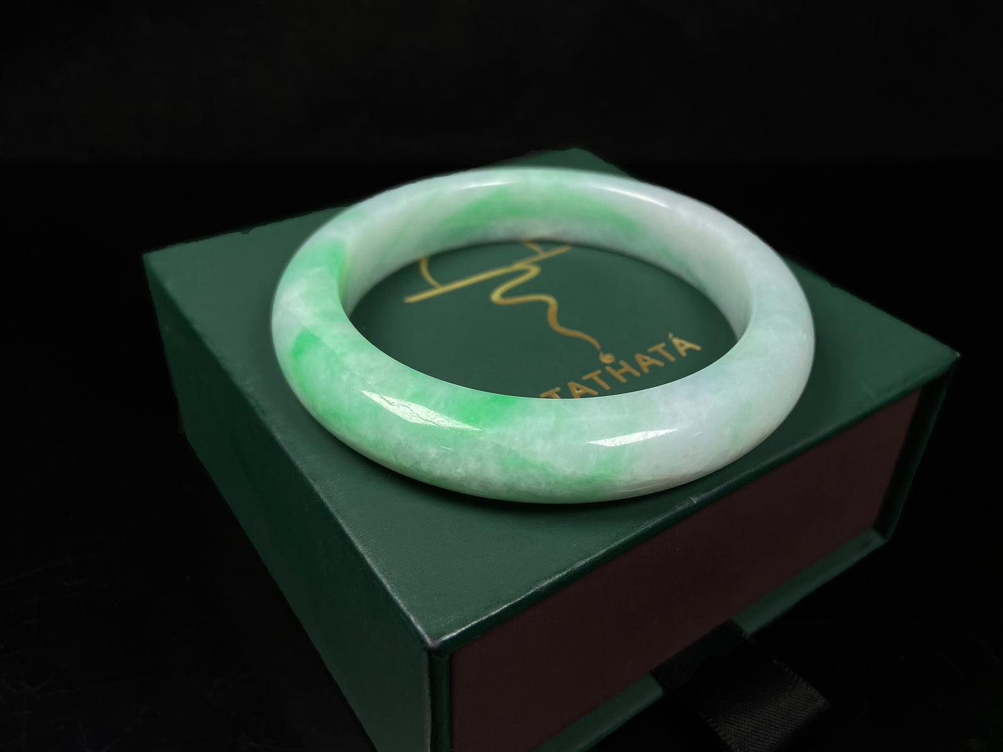 A white field with floating green hues jadeite bangle.