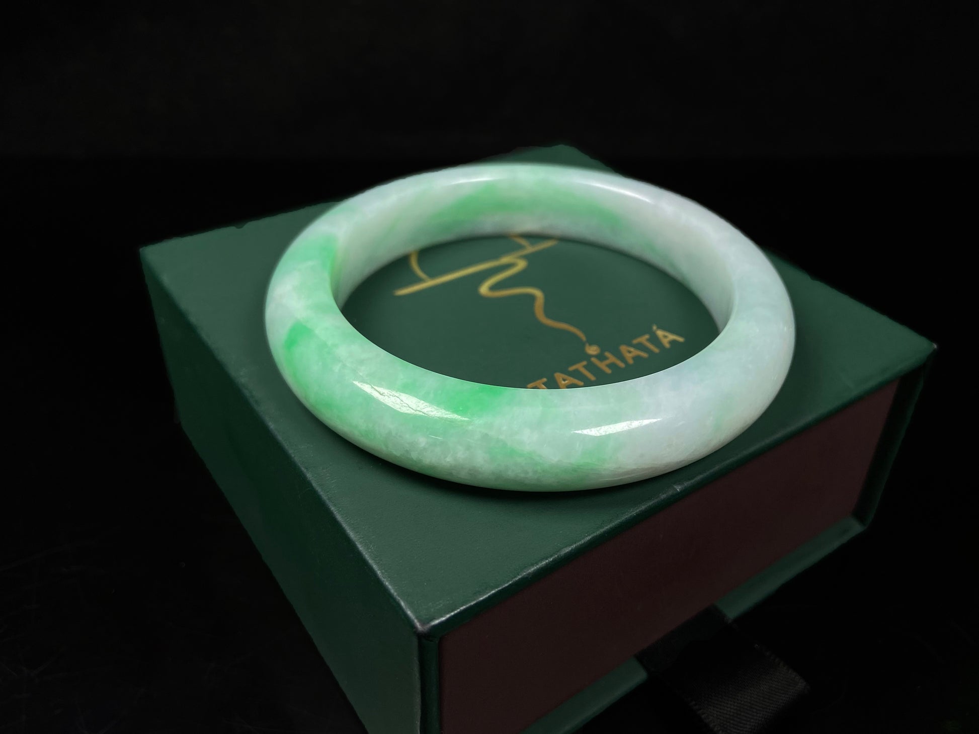 A white field with floating green hues jadeite bangle.
