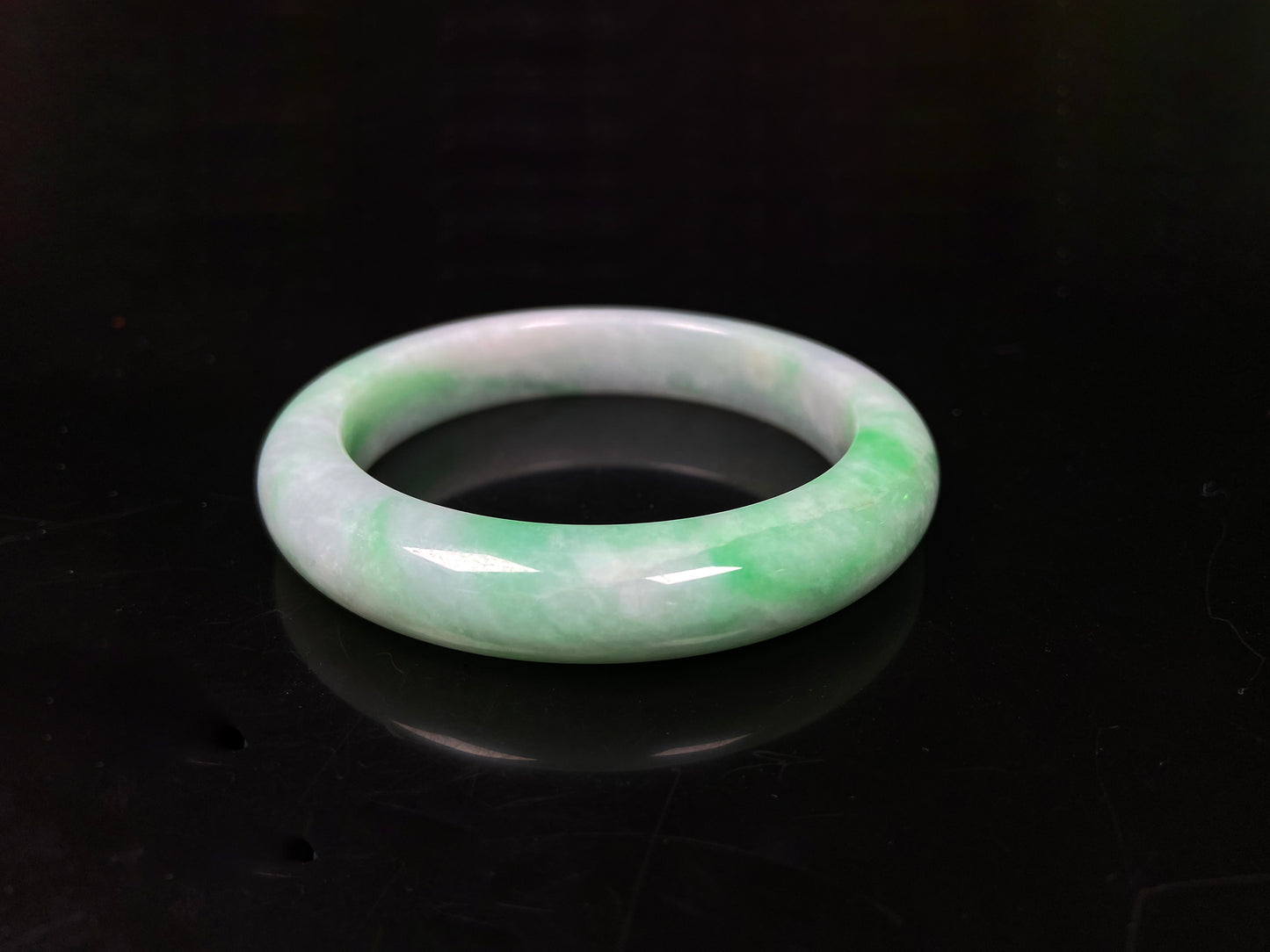 A white field with floating green hues jadeite bangle.