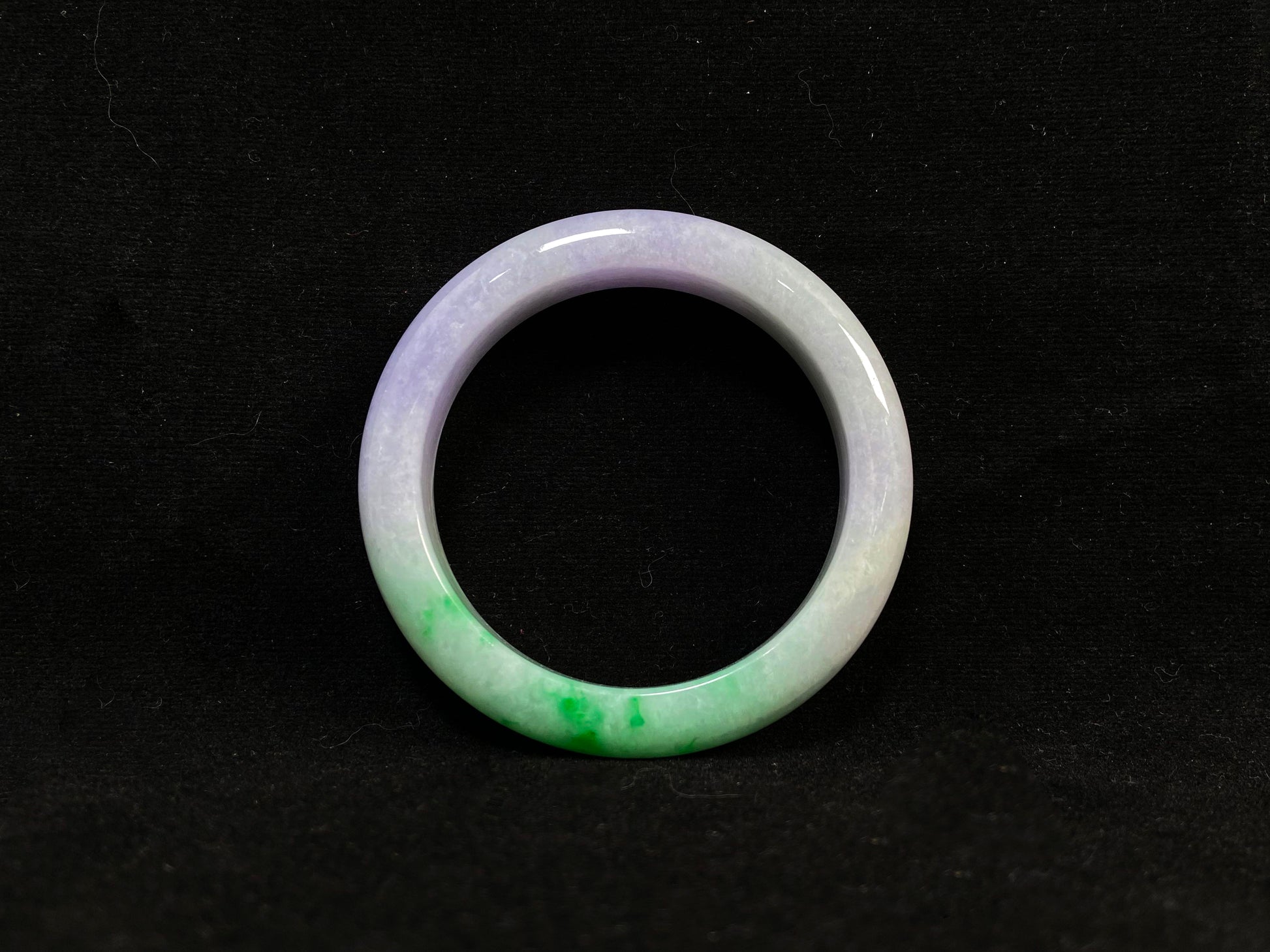 This natural jadeite bangle features a white base, elegantly divided into three sections: one in purple, one in green, and one in white with a subtle yellowish hue.