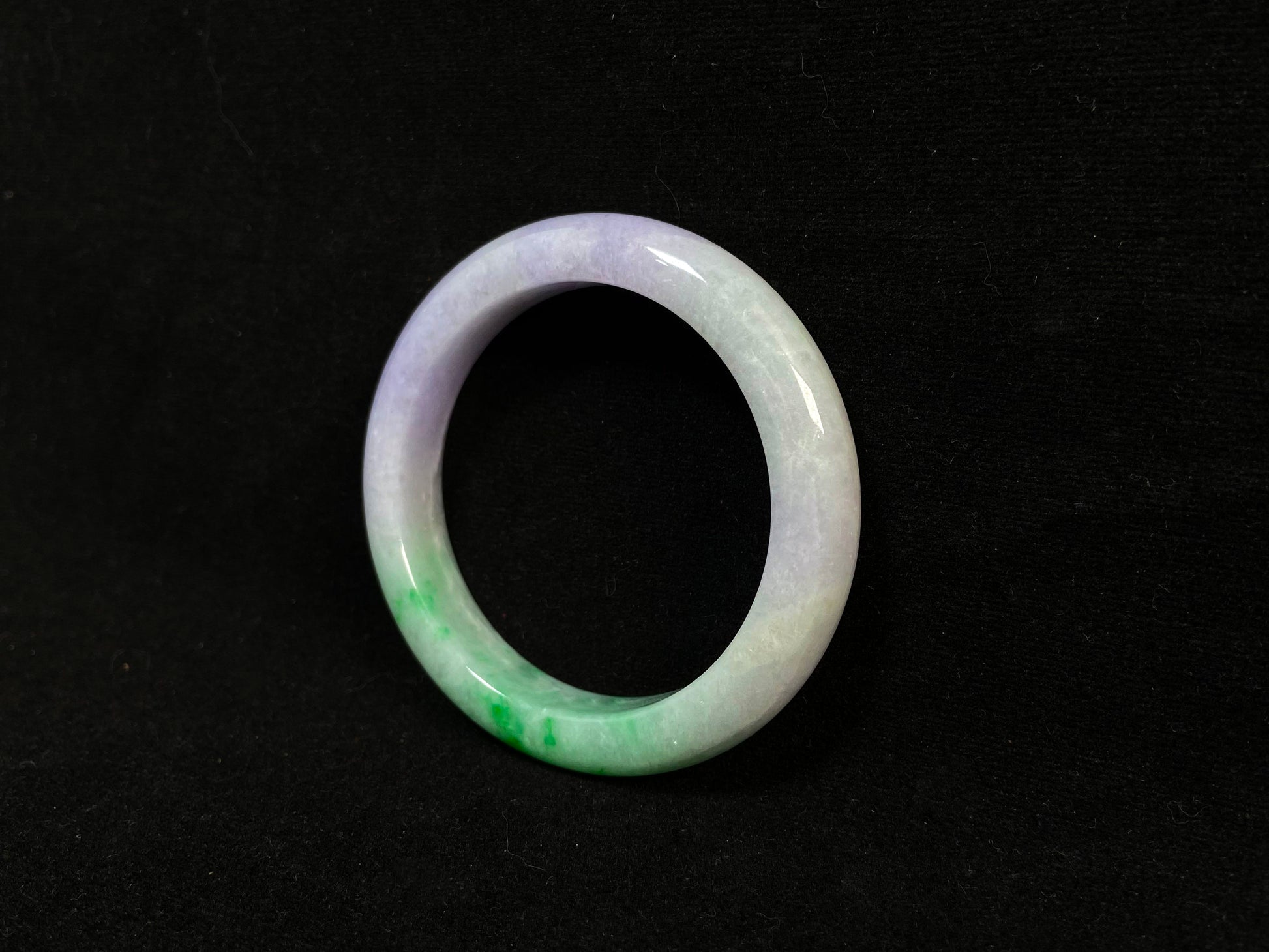 This natural jadeite bangle features a white base, elegantly divided into three sections: one in purple, one in green, and one in white with a subtle yellowish hue.