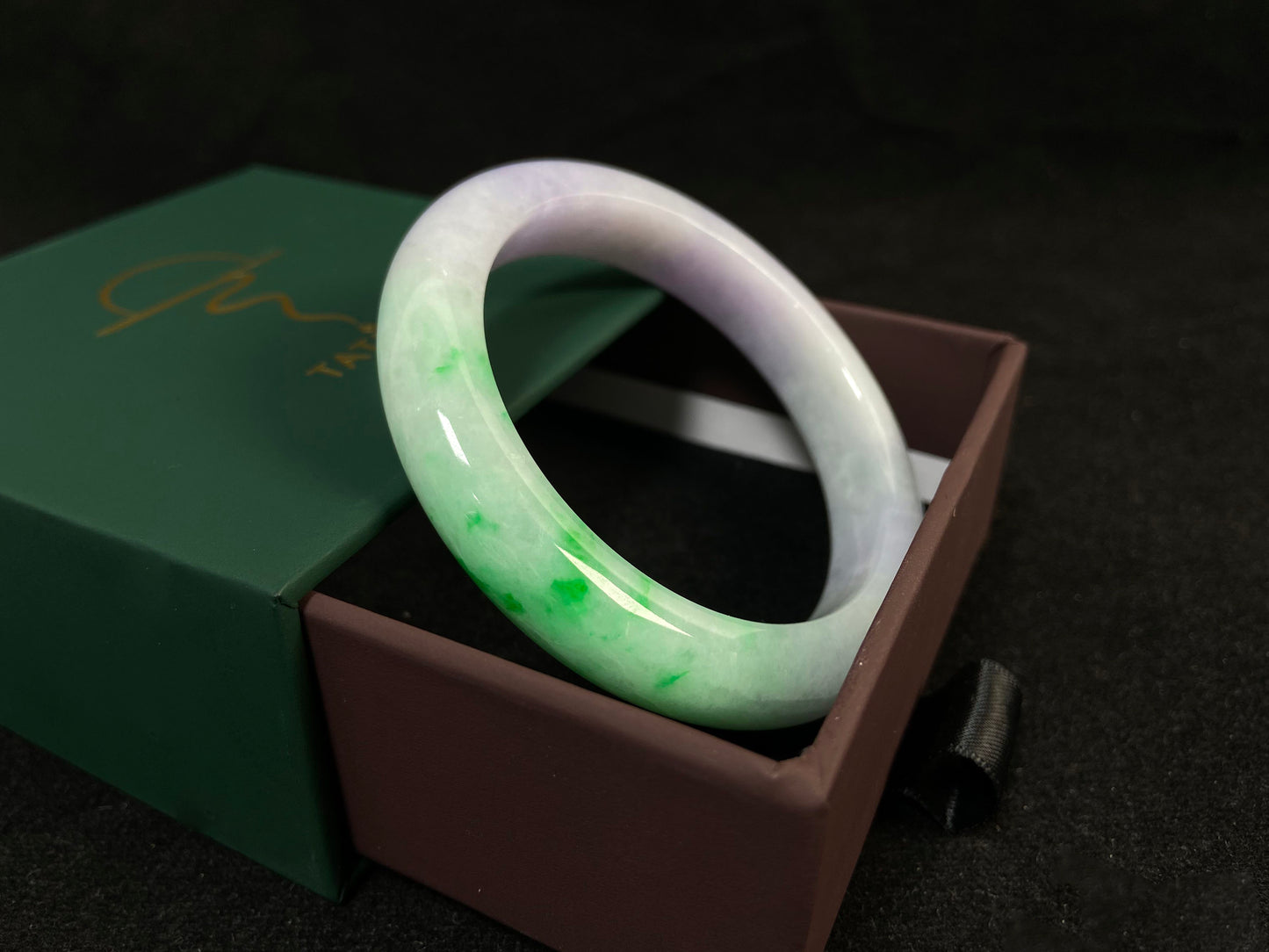 This natural jadeite bangle features a white base, elegantly divided into three sections: one in purple, one in green, and one in white with a subtle yellowish hue.