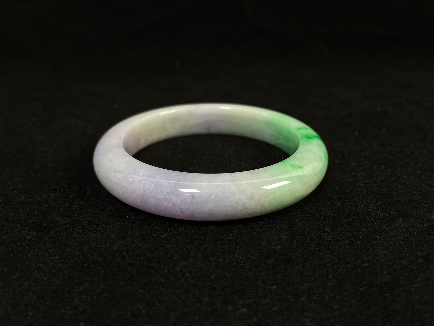 This natural jadeite bangle features a white base, elegantly divided into three sections: one in purple, one in green, and one in white with a subtle yellowish hue.