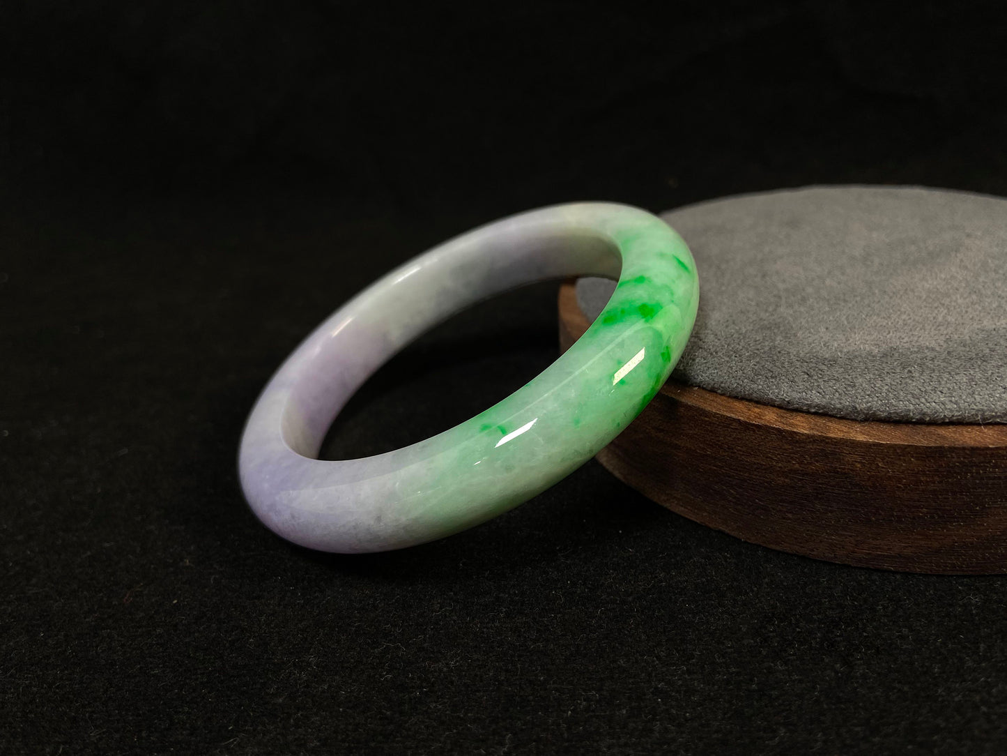 This natural jadeite bangle features a white base, elegantly divided into three sections: one in purple, one in green, and one in white with a subtle yellowish hue.