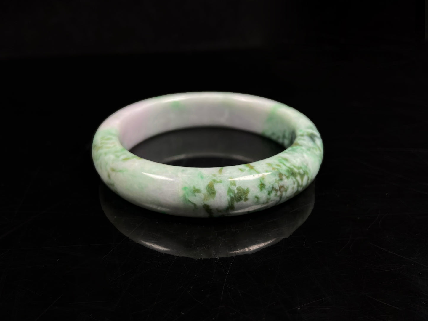 A white base with mottled green textures jadeite bangle.